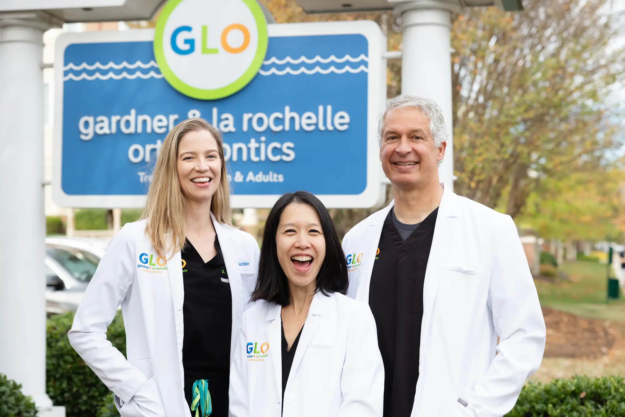 Dr. Gardner, Dr. La Rochelle and Dr. Tang in white coats in front of the Gardner & La Rochelle Orthodontics sign